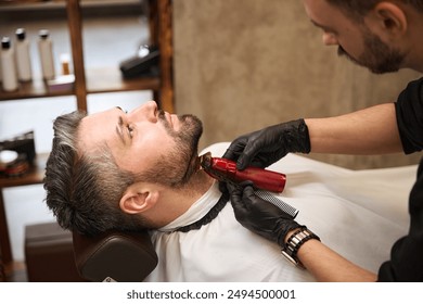 Focused barber trimming handsome man neck and beard, modeling the neckline