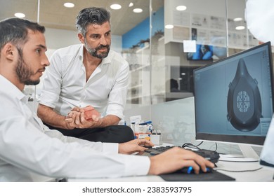 Focused bearded male engineers in formal wear browsing computer with 3d illustration of face mask in light office during coronavirus pandemic - Powered by Shutterstock