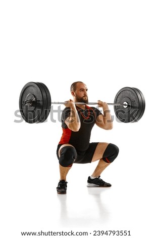 Focused bearded man, athlete with strong body training, lifting heavy weights, barbell against white background. Concept of sport, strength, gym, healthy lifestyle, power, endurance, weightlifting