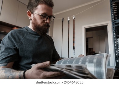 Focused bearded man intensely reviewing film negatives in a modern photography studio with equipment in the background. - Powered by Shutterstock