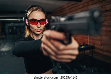 Focused Beautiful Shooter In Earmuffs Shooting A Handgun