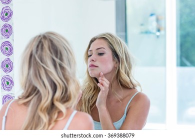 Focused beautiful young woman looking at herself in the bathroom mirror at home