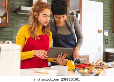 Focused biracial lesbian couple using tablet and preparing vegetables in kitchen. Communication, cooking, food, gay, relationship, togetherness, domestic life and healthy lifestyle, unaltered. - Powered by Shutterstock