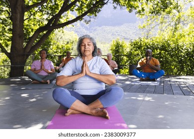 Focused biracial senior woman practising yoga with friends in sunny garden, copy space. Retirement, friendship, wellbeing and senior lifestyle, fitness and healthy lifestyle, unaltered. - Powered by Shutterstock