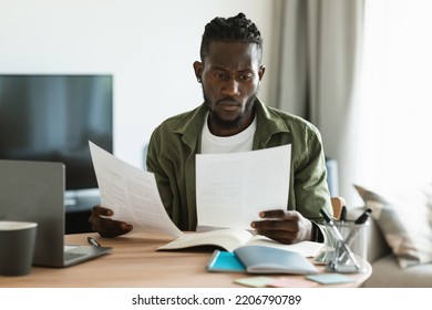 Focused Black Male Entrepreneur Reading Papers And Business Reports, Checking Documents While Sitting At Desk At Home. Entrepreneurship Career, Accounting And Documentation