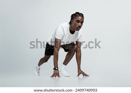 Focused black man in athletic wear poised in starting position for sprint, young african american runner guy exuding determination and strength, posing on light grey studio background, copy space