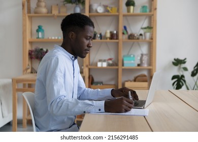 Focused Black Student Guy Watching Learning Webinar On Laptop, Writing Notes For Essay, Research Study. Freelance Business Professional Consulting Internet, Checking Legal Paper Document