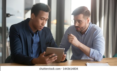 Focused Black And White Partners Colleagues Discussing Project Using Digital Tablet In Office, Male Diverse Executive Team Two Businessmen Coworkers Work In Teamwork Looking At Computer Sit At Desk