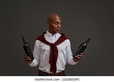 Focused black winemaker or sommelier holding and looking at wine bottle. Adult successful male entrepreneur. Viticulture and winemaking. Isolated on grey background. Studio shoot. Copy space