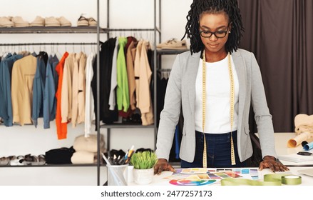 A focused black woman fashion designer stands at her work desk in studio, evaluating a variety of colorful fabric swatches. Surrounded by a diverse collection of garments and fashion accessories - Powered by Shutterstock