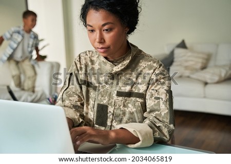 Focused black woman soldier using laptop at table