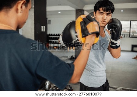 Focused boxer throws a powerful right hook into a focus mitt held by coach during boxing pad drills.