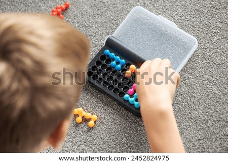 Focused boy deeply engaged in solving a colorful logic puzzle, enhancing his cognitive skills. Child development.