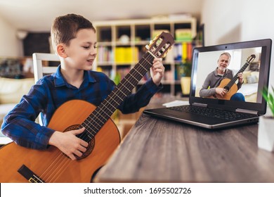 Konzentrierter Junge, der akustische Gitarre spielt und den Online-Kurs auf Laptop ansieht, während er zu Hause übt. Online-Schulung, Online-Kurse.
