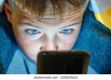 Focused boy under the blanket at night in his bed watching prohibited content.Child gadget addiction and insomnia.Selective focus.Close-up.
