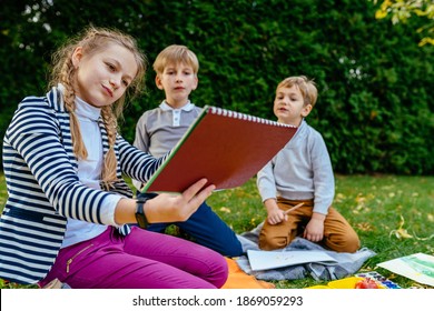 Focused boys an girl sitting on grass and drawing in park with pencil. Front view. Children outdoor activity concept. - Shutterstock ID 1869059293