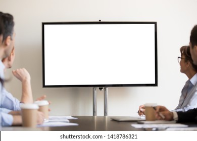 Focused business people gather at boardroom sitting at desk looking at tv white mock up with copyspace blank screen for advertisement. Seminar, presentation, corporate team at company training concept