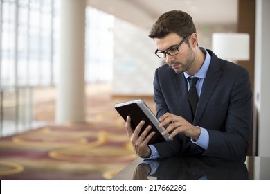 Focused businessman with glasses using smart electronic tablet at the hotel airport lobby checking stock market report
