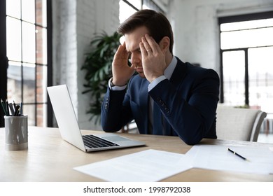 Focused businessman pondering on problem, thinking hard at workplace with laptop. Manager trying to cope with headache and fatigue, suffering from migraine, feeling stress, rubbing head. - Shutterstock ID 1998792038
