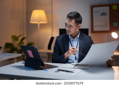 Focused businessman reviewing documents and using digital tablet while working late in a dimly lit office - Powered by Shutterstock