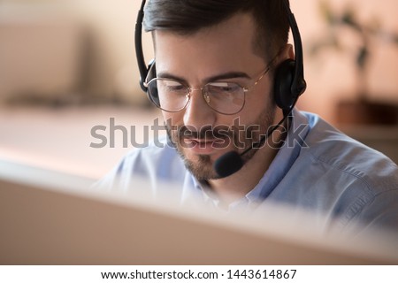 Focused businessman telemarketer telesales agent wear wireless headset make conference video call talk consult online client on computer, male helpline operator work in customer care support office