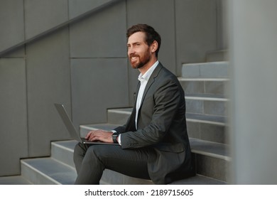 Focused Businessman Working On Laptop Sitting On Stairs Outside Office Building 