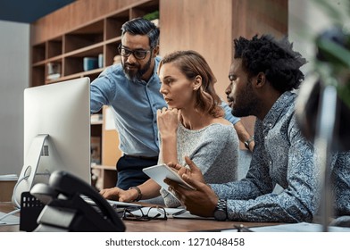 Focused businesspeople discussing project while looking at computer screen. Mature manager working with his creative team in a modern office. Multiethnic casual teamwork at work. - Powered by Shutterstock