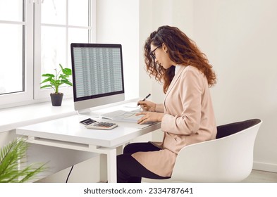 Focused businesswoman analyzing financial spreadsheet report on computer screen. Accountant, analyst, financial manager checking electronic spreadsheet and doing paperwork on office