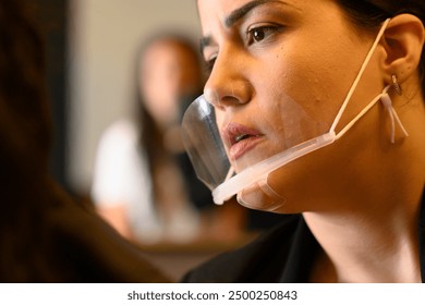 Focused businesswoman in an office wears a clear face mask, talking with colleagues. Lip reading and facial expressions are visible, promoting inclusive communication - Powered by Shutterstock