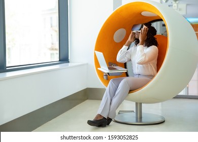 Focused businesswoman in VR headset using laptop. Full length view of young African American businesswoman wearing virtual reality headset and using laptop computer in office. Technology concept