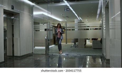 Focused Businesswoman Walking Office Corridor, Corporate Manager Using Smartphone On The Go. Business Woman Hand Pressing Lift Button. Serious Lady Entering Elevator In Modern Building