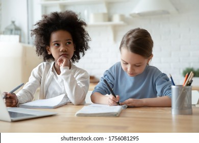 Focused Busy Little Schoolgirls Multi Ethnic Sisters Do Homework Writing Thinking Seated At Table In Kitchen. Homeschooling During Quarantine, Self-education, Gain New Knowledge, Brain Work Concept