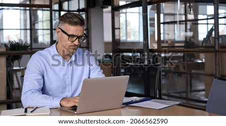 Focused busy mature business man lawyer ceo trader using computer, typing, working in modern office room doing online data market analysis, thinking planning tech strategy looking at laptop.