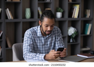 Focused Busy Millennial Black Business Man Browsing Internet On Smartphone, Using Online App, Reading Text Message, Sitting, Working At Home Office Workplace Table, Making Telephone Call