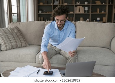 Focused busy young entrepreneur man using calculator at home, checking legal documents, domestic paper bills for payment, counting investment, income, doing accounting job - Powered by Shutterstock