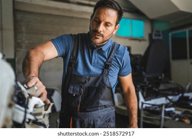 A focused car mechanic inspects machinery in a workshop, wearing a blue polo shirt and dark overalls, with a backdrop of various automotive tools and equipment - Powered by Shutterstock