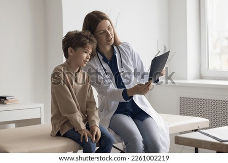 Focused caring family doctor woman and patient kid watching Xray scan, shot of bones, radiography screening films. Boy visiting pediatrician for medical checkup, diagnosing trauma, illness