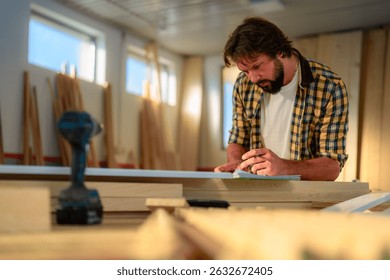 Focused carpenter meticulously taking notes and planning his woodwork project in a bright and organized workshop, surrounded by tools and lumber