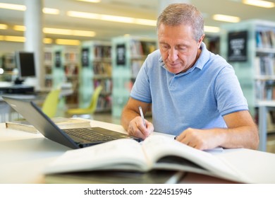 Focused Casual Mature Male Writing In Notepad And Reading Books In The Library. High Quality Photo