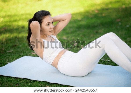 Focused caucasian woman athlete in white activewear doing crunches on a yoga mat in a park, engaging her core muscles during an outdoor workout session with a watch, outside [[stock_photo]] © 