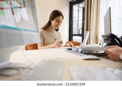 Focused Charming Caucasian Woman Filling Out Questionnaire Or Paper Documents While Sitting At The Reception Desk Of A Medical Clinic Or An Office Building Of Social Security Financial Aid Department