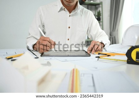 Focused civil engineer man using digital tablet, inspecting construction plan at his workstation