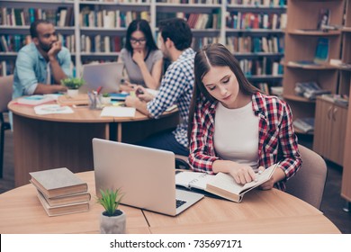Focused concentrated attractive clever female student is learning with thesaurus in hard bookcase, wearing casual checkered shirt, behind her are classmates, book shelves of campus library - Shutterstock ID 735697171