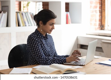 Focused Confident Indian Female Student Sitting In Library, Studying With Books And Computer, Searching Scientific Article Or Educational Information, Attending Online Course, Preparing For Session.