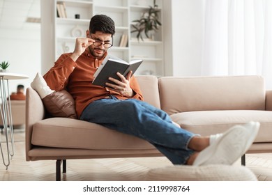 Focused confused young Arabic man trying to read paper book, squinting to see more clearly, wearing glasses, having difficulties seeing text because of vision problems, sitting on couch in living room - Powered by Shutterstock - Get 15% off with code: PIKWIZARD15