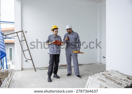 Focused construction worker and builder engineer wearing hardhat discuss teamwork looking clipboard building site. Professional team planning project inside uncompleted interior architecture