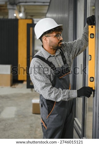 Focused construction worker checking vertical alignment of modular house wall using spirit level, ensuring precise and quality building assembly