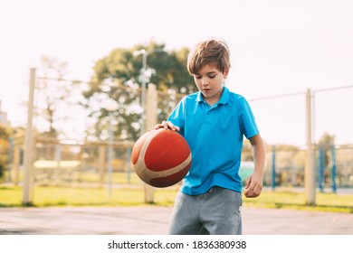 Focused Cute Boy Athlete Leads The Ball In A Game Of Basketball. A Boy Plays Basketball After School. Sports, Healthy Lifestyle, Leisure