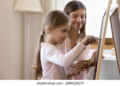 Focused cute girl kid learning to write, drawing with chalk on chalkboard under control of daycare teacher. Happy mom and daughter kid studying in game at home, enjoying education activity - Shutterstock ID 2089628275