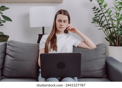 Focused cute young caucasian woman sitting alone on cozy sofa working on laptop. Freelancer in calm and cozy living room coding. Remote working in comfortable environment. Business concept - Powered by Shutterstock